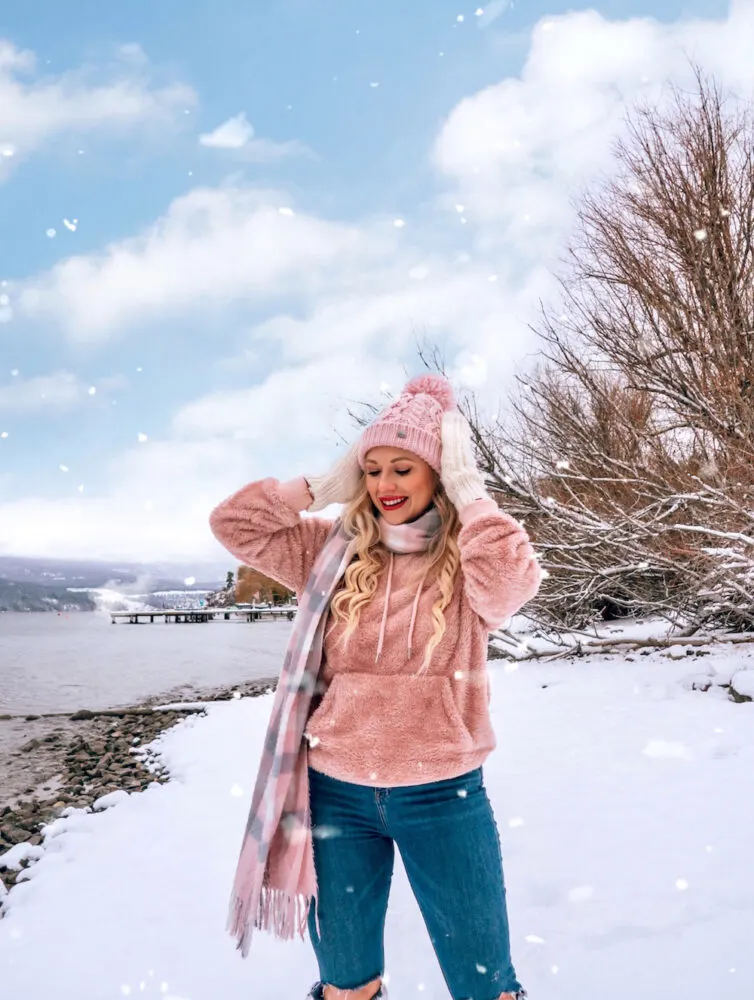 Young trendy woman in winter outfit posing under snowfall near