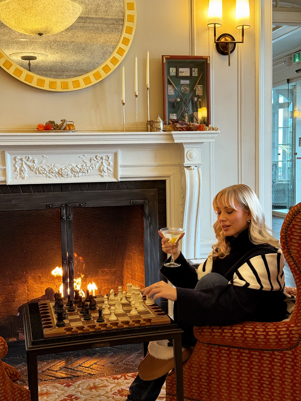 Guest relaxing by the fireplace at the Algonquin Resort with a martini and a game of chess during a fall getaway.