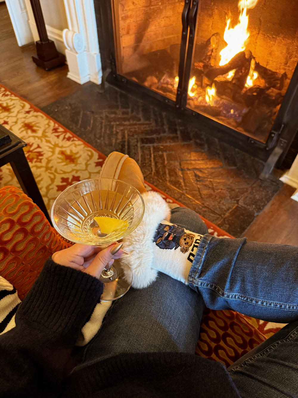 Guest relaxing by the fireplace at the Algonquin Resort in St. Andrews by-the-Sea, New Brunswick, sipping a cocktail on a cozy fall evening.