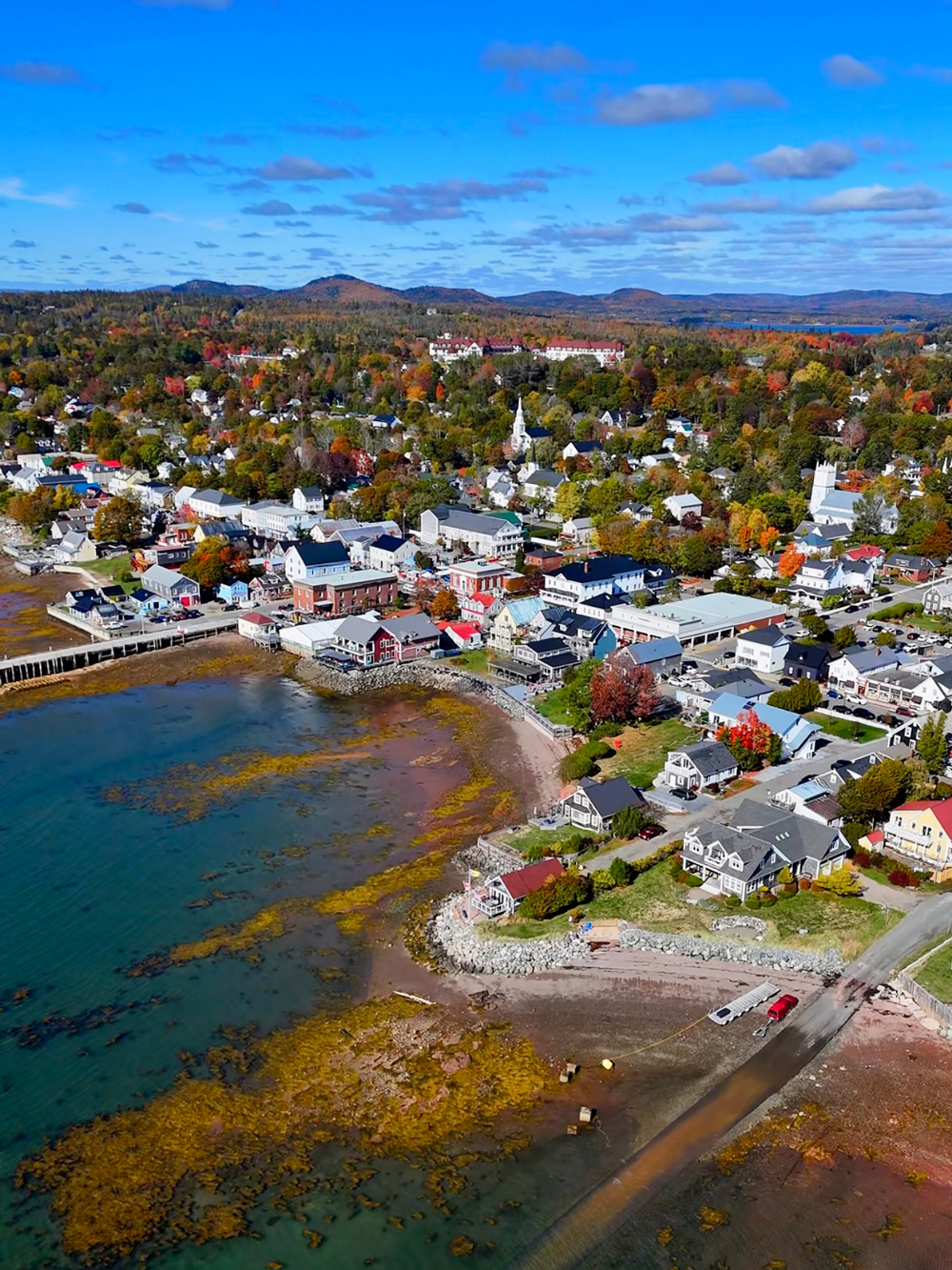 Aerial drone photo of downtown St. Andrews by-the-Sea, New Brunswick, showing the colourful coastal town, Bay of Fundy shoreline, and harbour views near the Algonquin Resort.