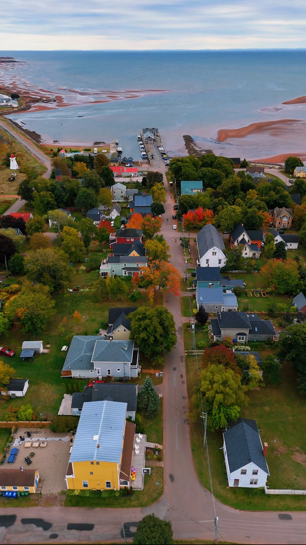 Coastal scene in Victoria-by-the-Sea, PEI &mdash; red cliffs, colorful fishing shacks, and lighthouse views on a crisp fall day.