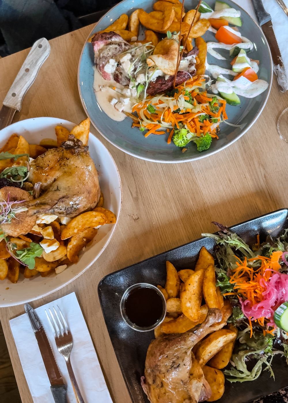 Table filled with hearty winter dishes at Bistro Montebello, including duck confit poutine, roasted chicken, potatoes, and fresh salads.