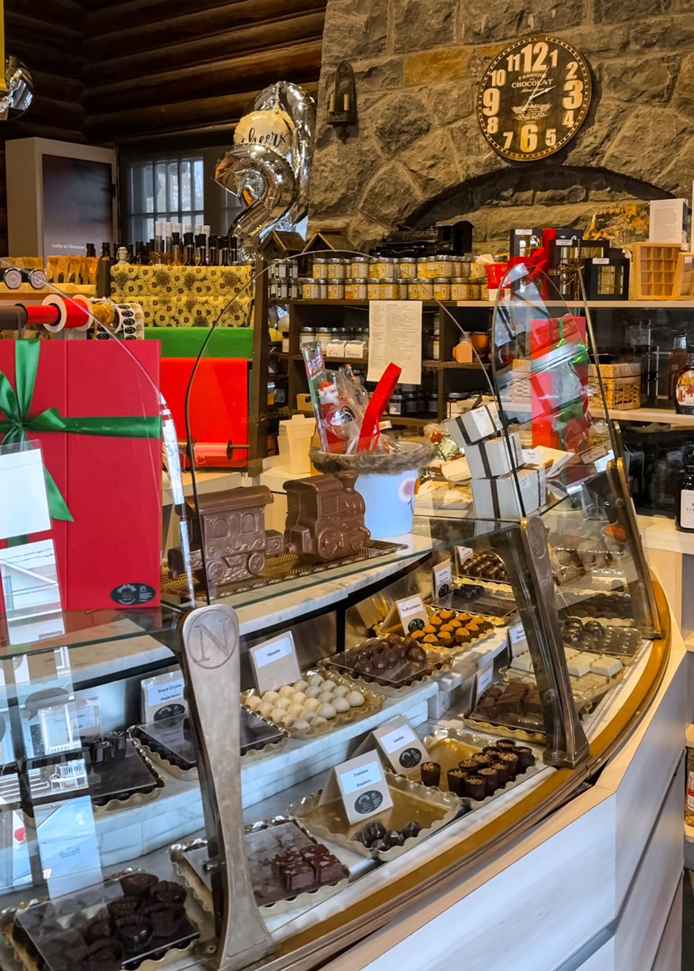Inside ChocoMotive Montebello, showcasing artisanal chocolates, festive gift boxes, and holiday treats displayed inside a rustic stone chocolate shop.