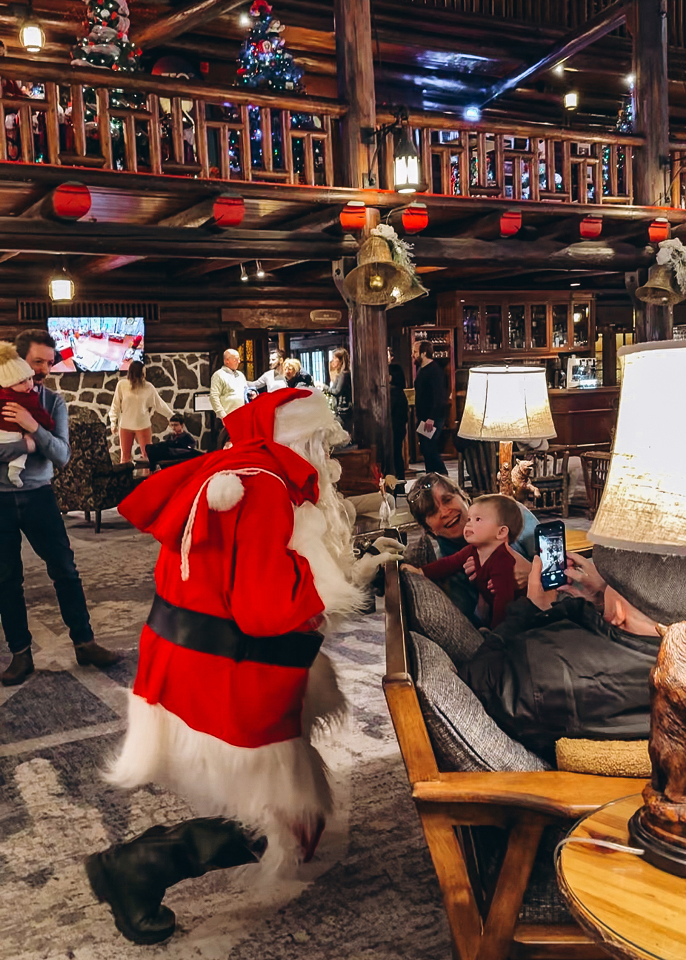 Santa Claus greeting a child inside the festive lobby of Fairmont Montebello, surrounded by Christmas decorations and families enjoying the holidays.