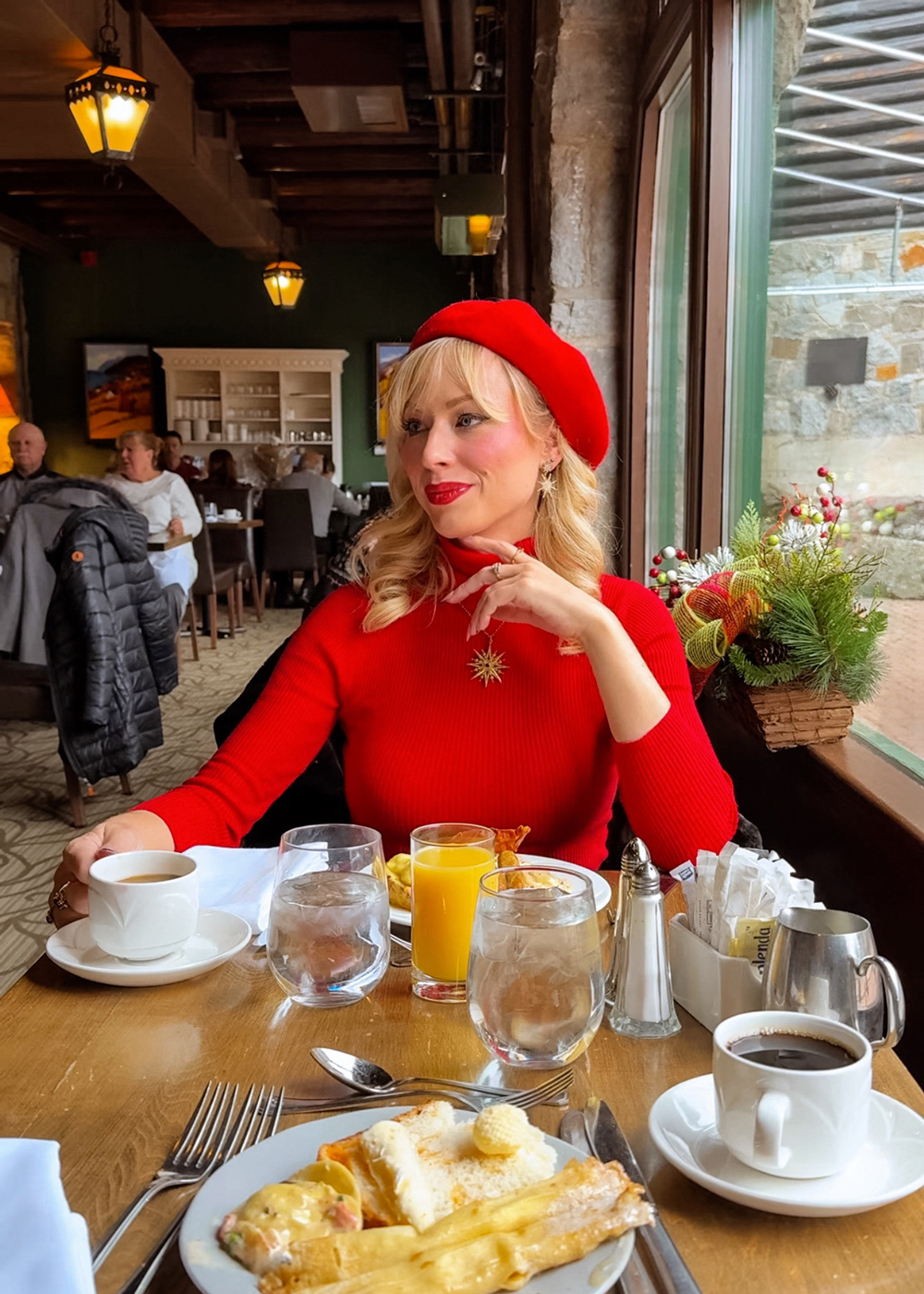 Woman in a red beret enjoying brunch at Aux Chantignoles at Fairmont Montebello, with plates of breakfast food, coffee, and juice on the table.