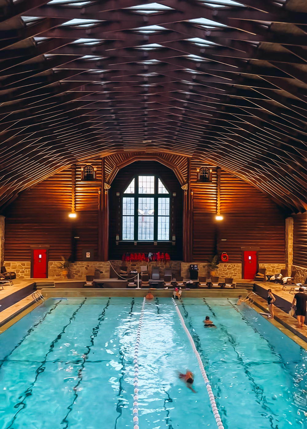 Indoor pool at Fairmont Le Ch&acirc;teau Montebello inside the historic log-cabin sports complex, with guests swimming beneath arched wooden beams.