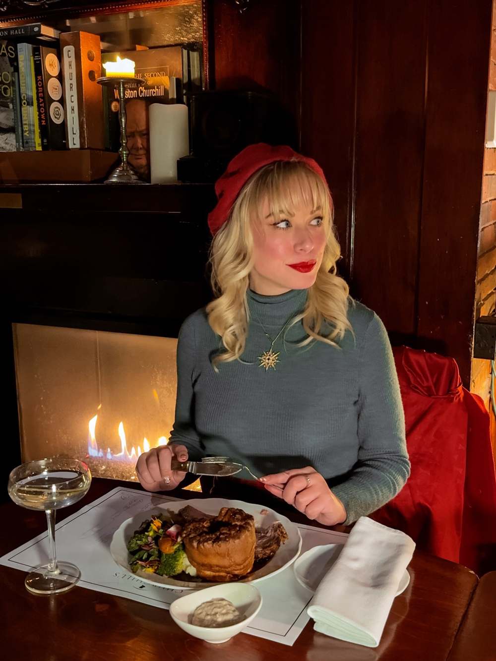 Woman in a red beret enjoying a roast dinner beside a fireplace at Churchill&rsquo;s restaurant in North Bay.