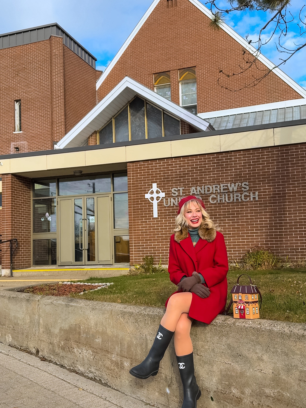 Woman in a red coat and beret sitting and smiling outside St. Andrew&rsquo;s United Church in North Bay, a filming location featured on the North Bay Hallmark movie tour.