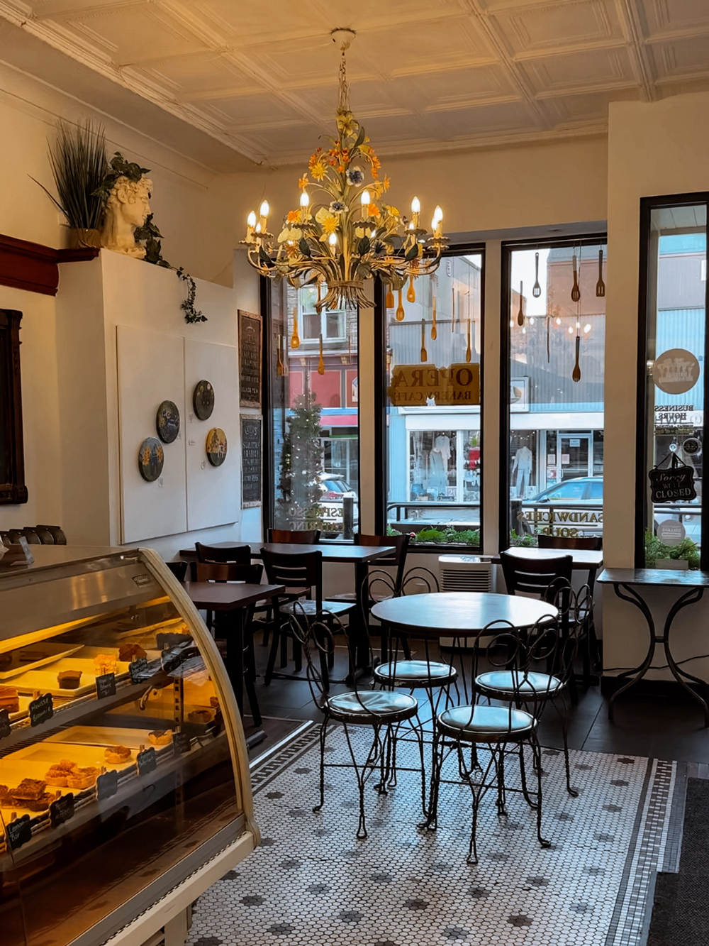 Cozy caf&eacute; interior with vintage-style chandelier, bistro tables, and a pastry display case.