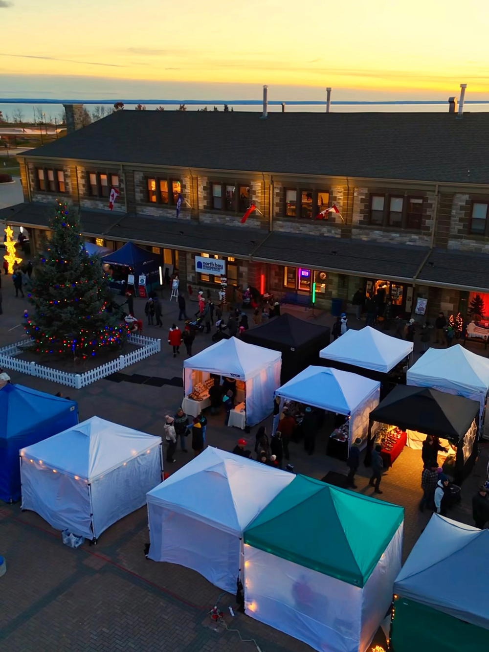 Vendor tents clustered around the waterfront with the historic station building and Christmas lights at dusk.