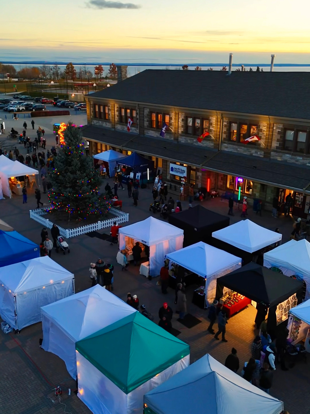 Overhead view of North Bay&rsquo;s Winter Market with vendor tents and a lit Christmas tree at sunset.