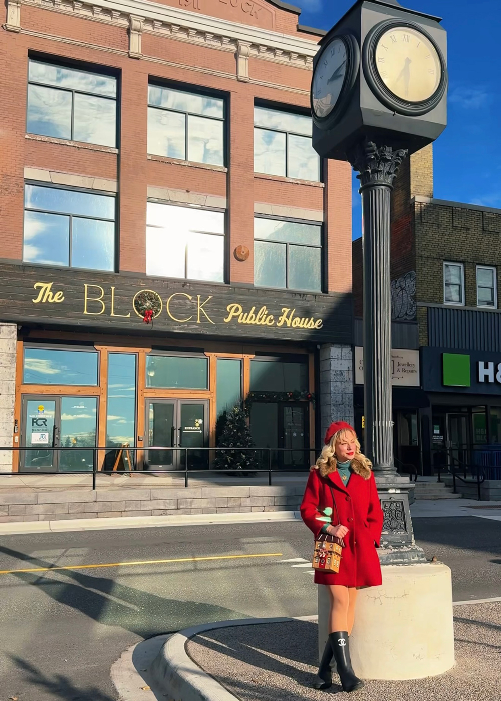 Woman in a red coat standing beside a street clock outside The Block Public House in downtown North Bay.