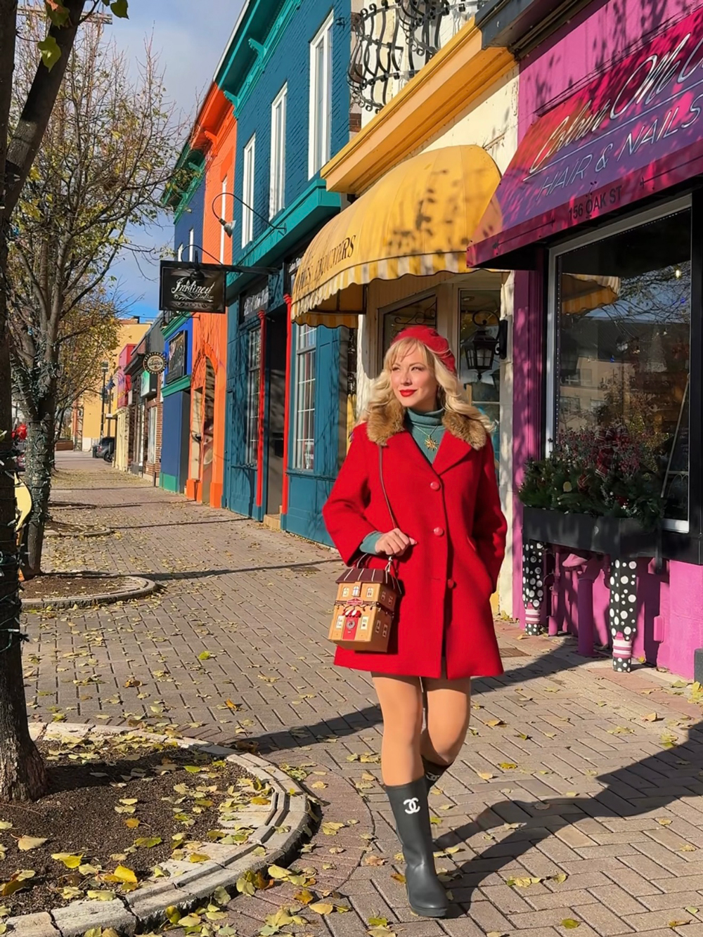 Woman in a red coat walking past vibrant storefronts under yellow and purple awnings.