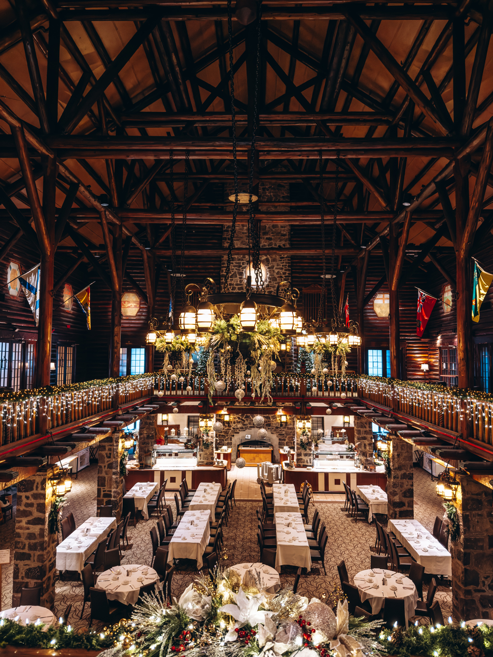 Large festive dining hall at Fairmont Le Ch&acirc;teau Montebello decorated with Christmas garlands, twinkle lights, and long banquet tables set for a holiday meal.