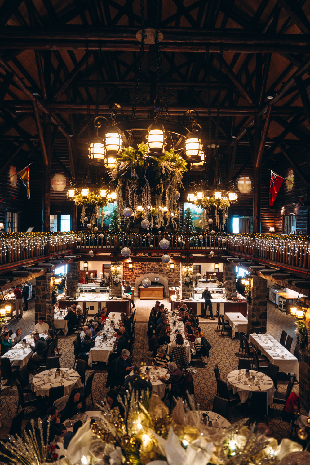 Holiday brunch scene inside Aux Chantignoles at Fairmont Montebello, with guests dining beneath Christmas chandeliers, garland-wrapped railings, and warm log-cabin d&eacute;cor.