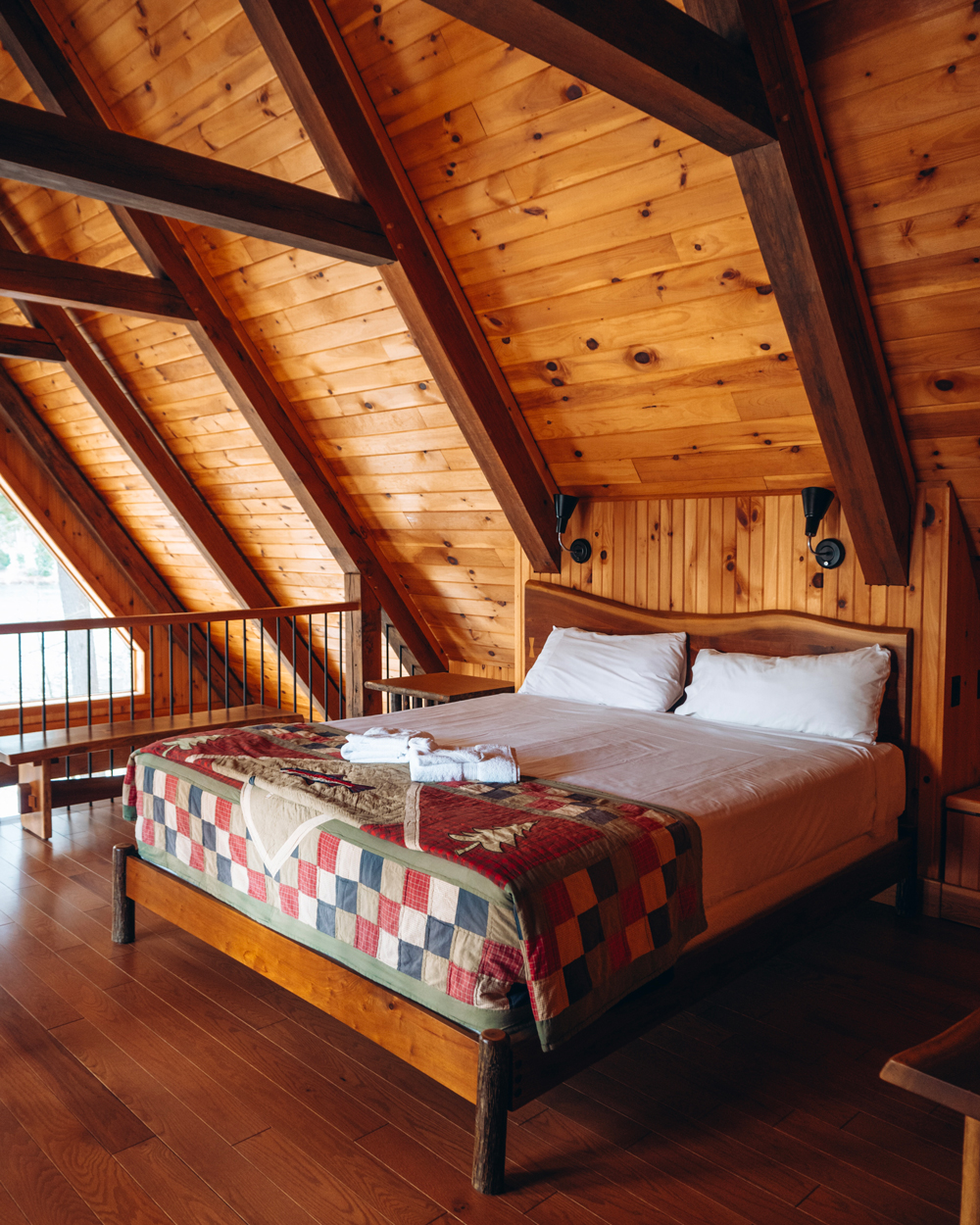 A cozy bedroom inside a Kenauk Nature chalet with wood-paneled walls, exposed beams, and a patchwork quilt on the bed.