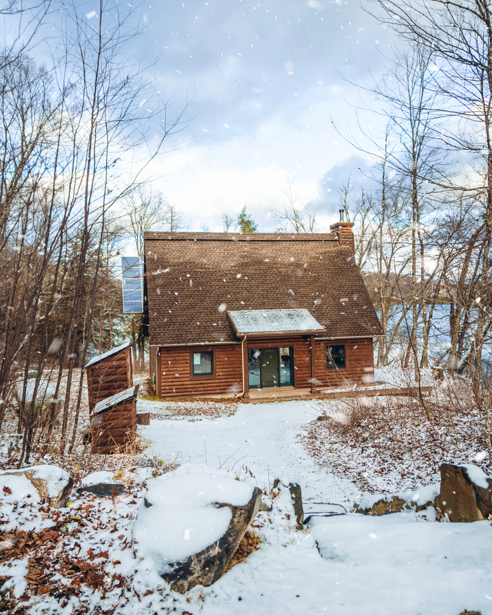 Exterior of a Kenauk Nature chalet surrounded by light snowfall and winter forest scenery.