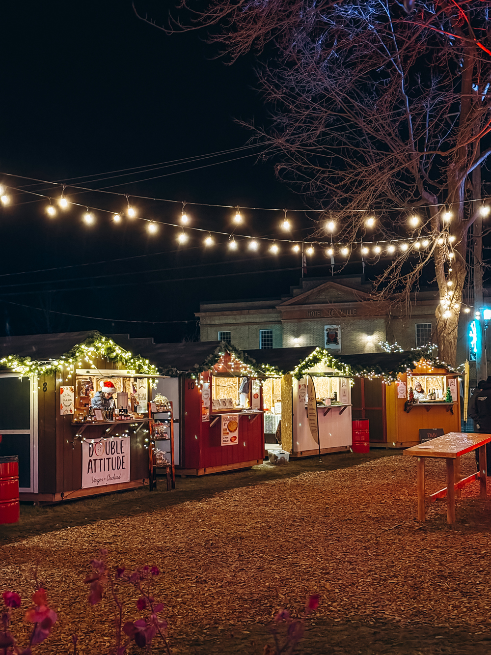 Festive wooden vendor stalls decorated with garlands and lights at the Montebello Christmas Market at night.