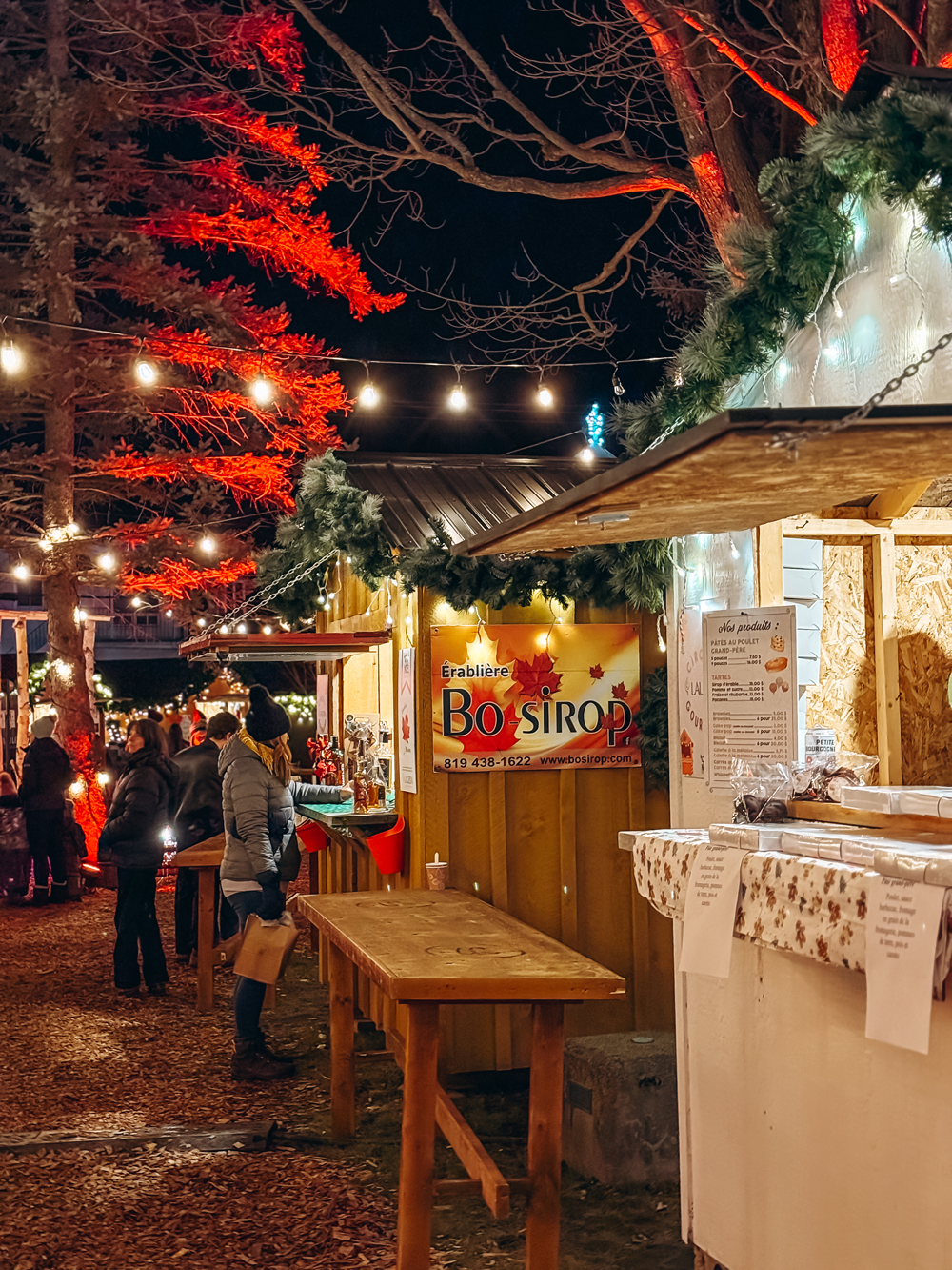 A row of Christmas market stalls illuminated by string lights at night at the Montebello Christmas Market.